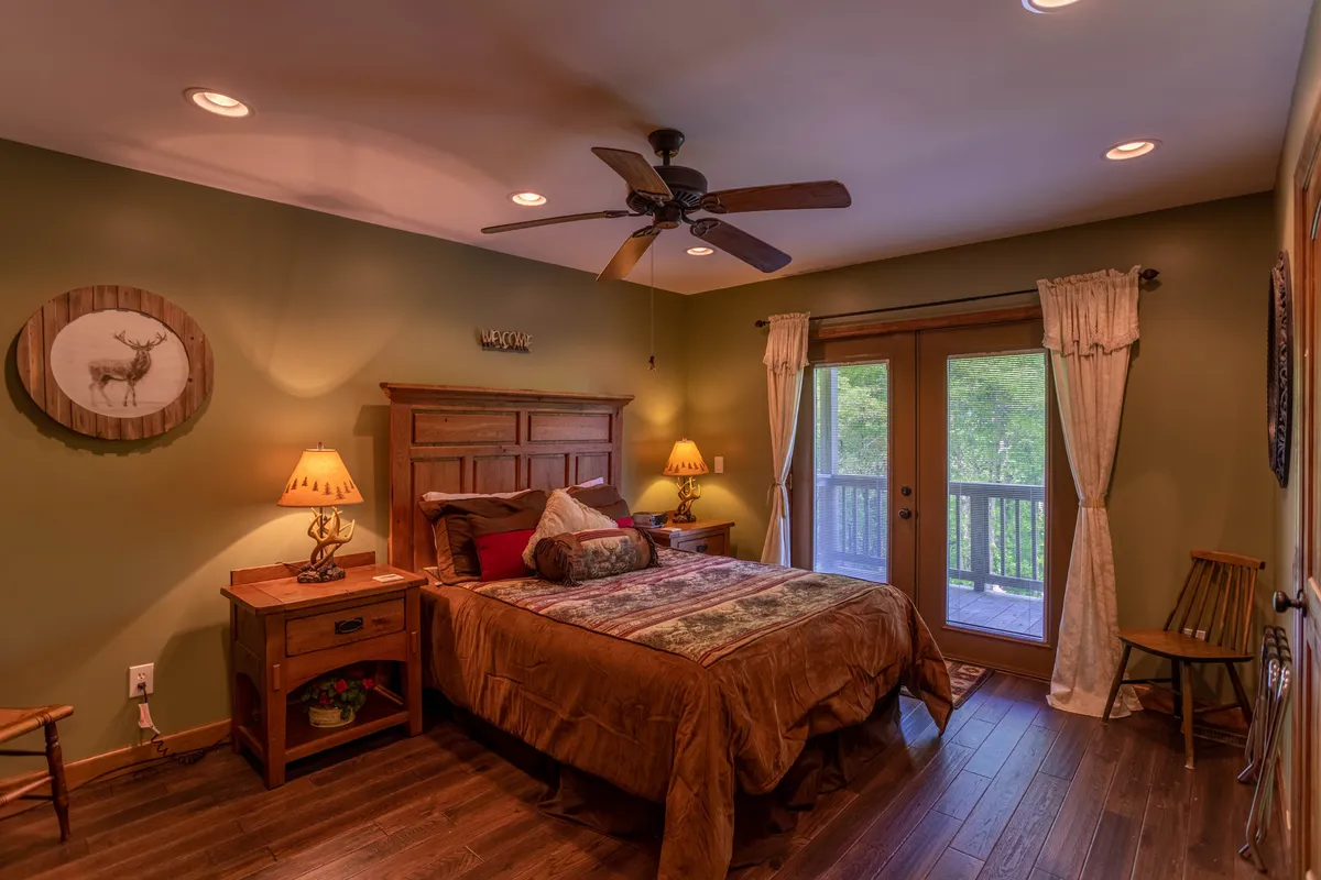 A welcoming bedroom with a wooden bed frame, plush pillows, lamps, and a sliding glass door that opens to nature. The room exudes peace, with soft natural light and calming colors.