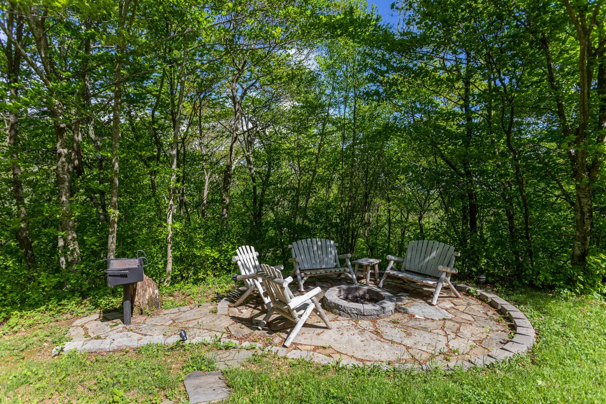 An inviting fire pit area, complete with Adirondack chairs and a grill, sits outdoors against a natural backdrop. The setting is ideal for gathering with friends and family, stargazing, or warming up after snowy adventures.