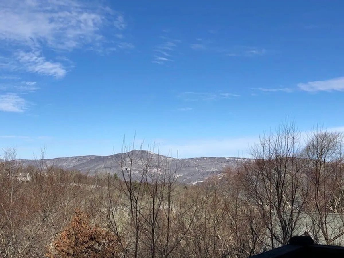 A sweeping vista of distant mountain ranges under a clear blue sky is framed by bare trees. The landscape suggests openness and tranquility, with plenty of space for hiking, bird watching, and appreciating the natural beauty. The image invites viewers to imagine themselves exploring the trails and soaking in the expansive views.